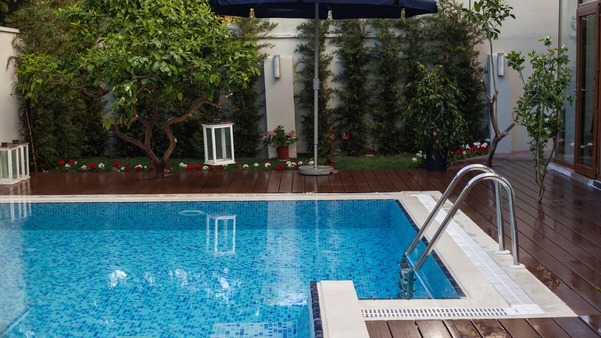 A clear backyard pool with a ladder, a wood deck and a patio umbrella