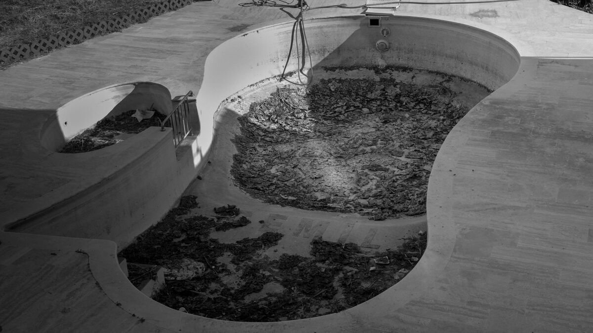 A drained kidney-shaped pool with its old plaster exposed, ready for resurfacing