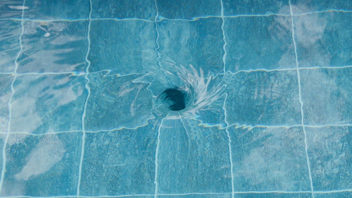 Water swirling down a drain in a pool floor of square tiles